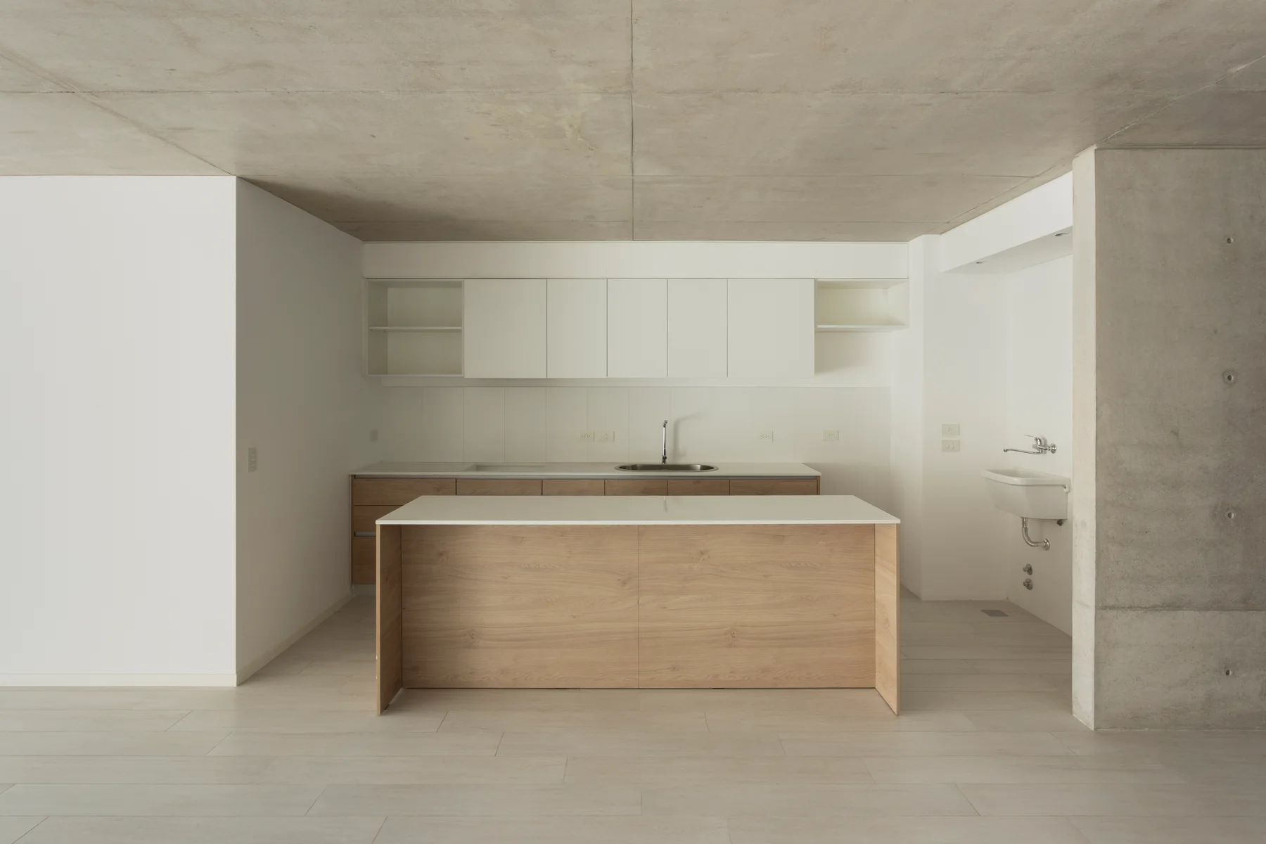 Cocina integrada con isla, muebles blancos y terminaciones en tono madera